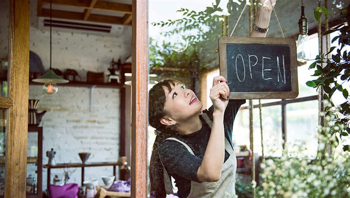 woman opening her store hanging open for business sign.jpg